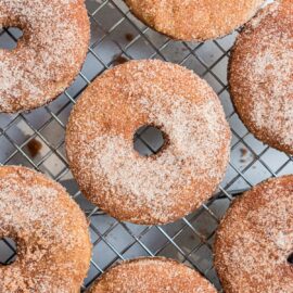 Apple cider donuts with cinnamon sugar coating on wire rack.