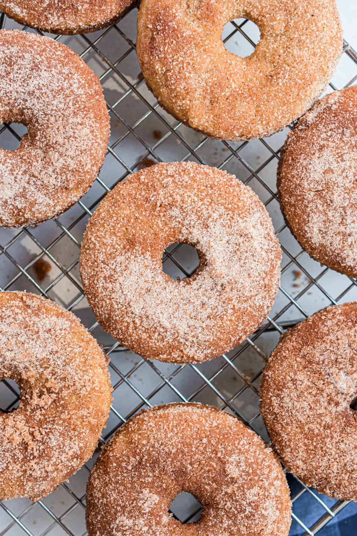 Apple cider donuts with cinnamon sugar coating on wire rack.