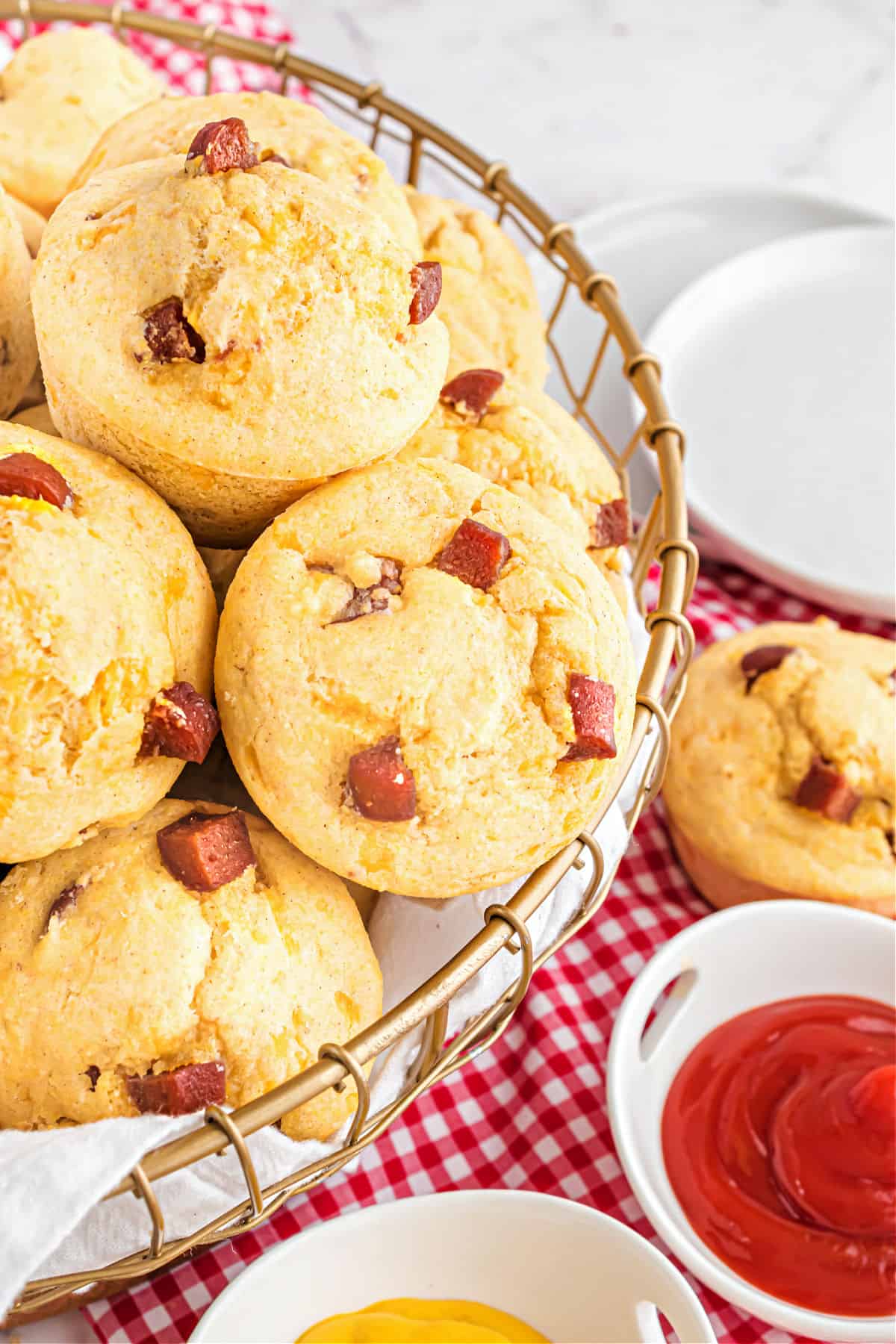 Corn dog muffins in wire basket with sides of ketchup and mustard for dipping.