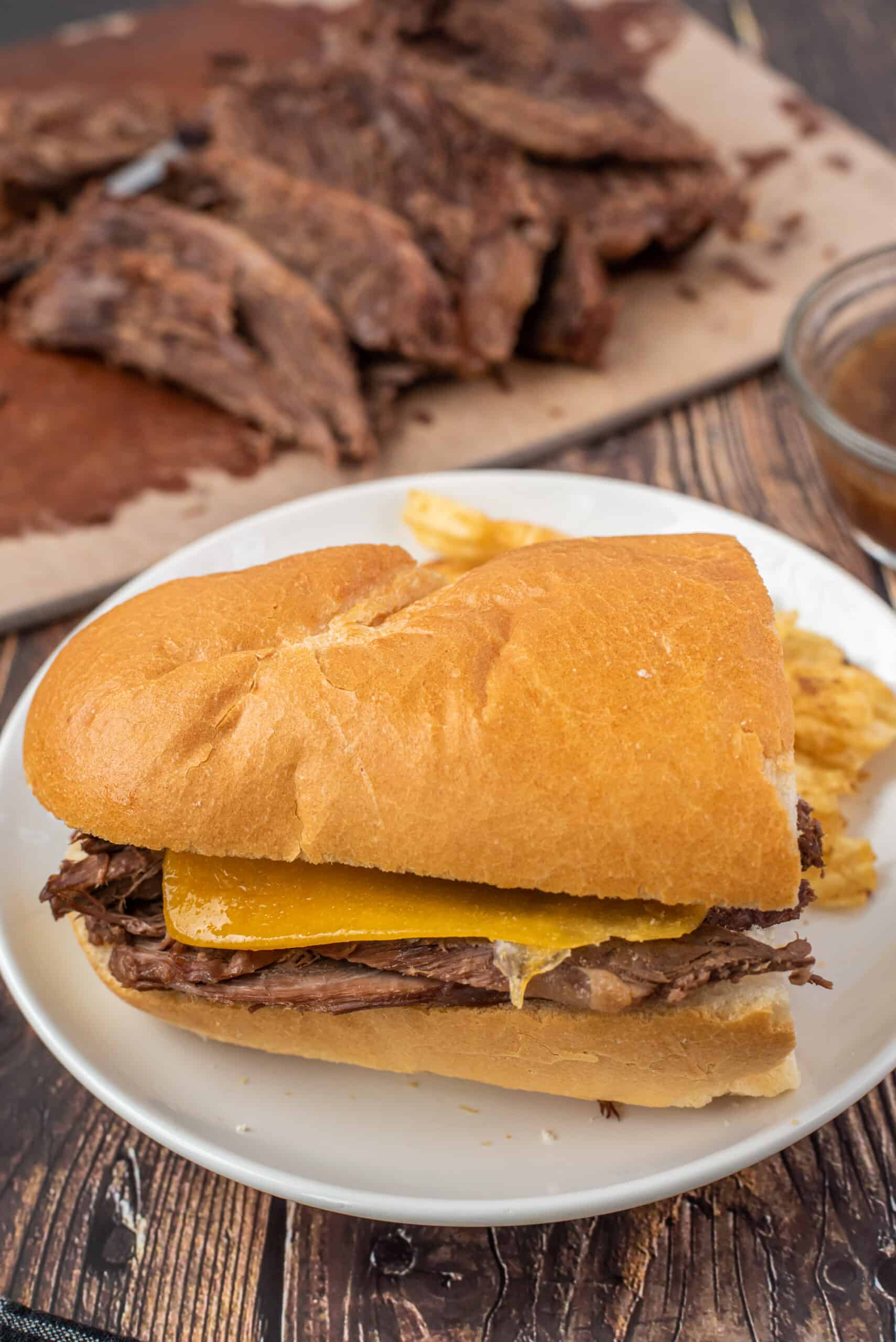 French Dip sandwich on baguette with sliced beef in background.