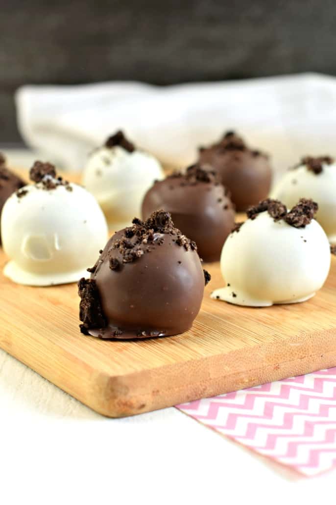 Wood cutting board topped with dark chocolate and white chocolate oreo peanut butter balls.