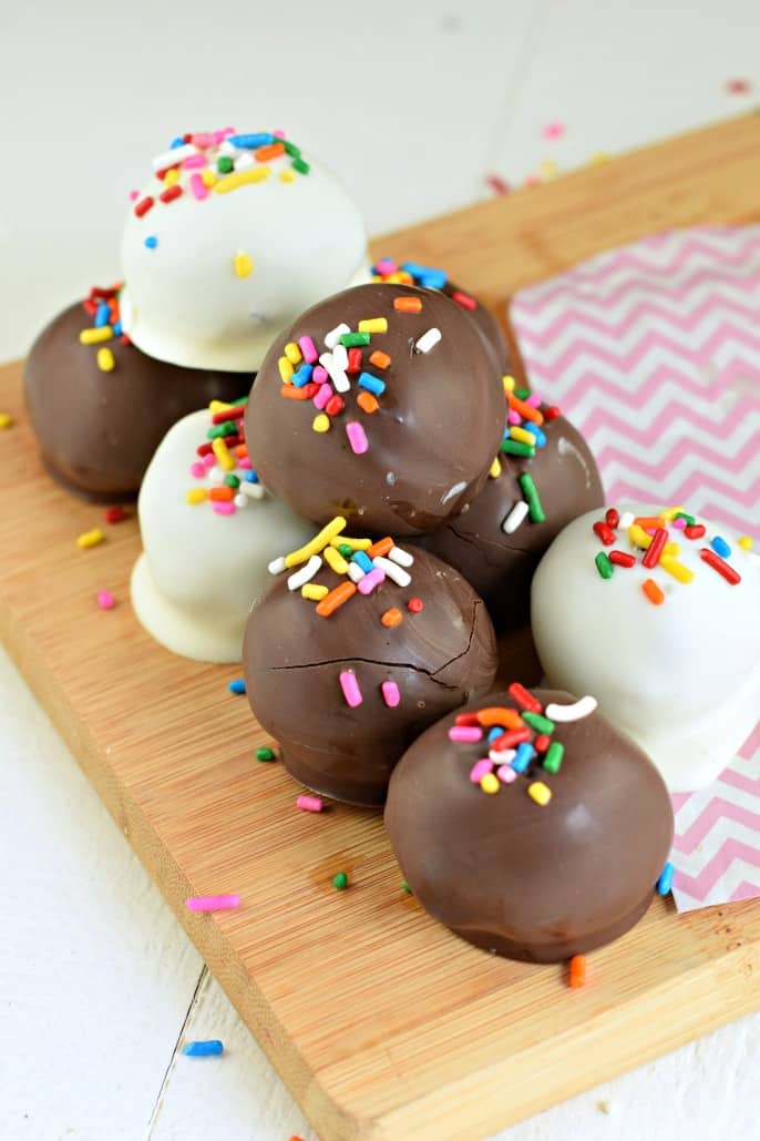 Oreo peanut butter truffles dipped in white chocolate and dark chocolate and topped with colorful sprinkles, on a wooden cutting board.