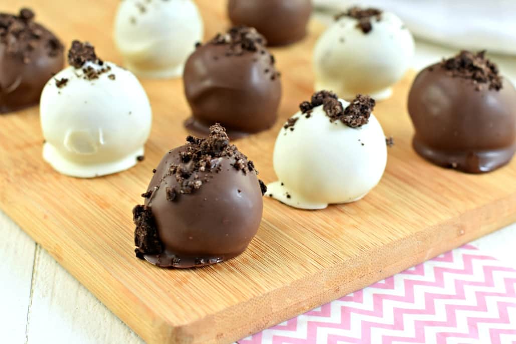 Homemade truffles with oreo and peanut butter dipped in dark chocolate and white chocolate on a wooden cutting board.