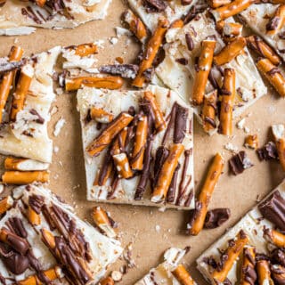 Pieces of white chocolate candy with salted caramel, pretzels, and milk chocolate drizzled on top.