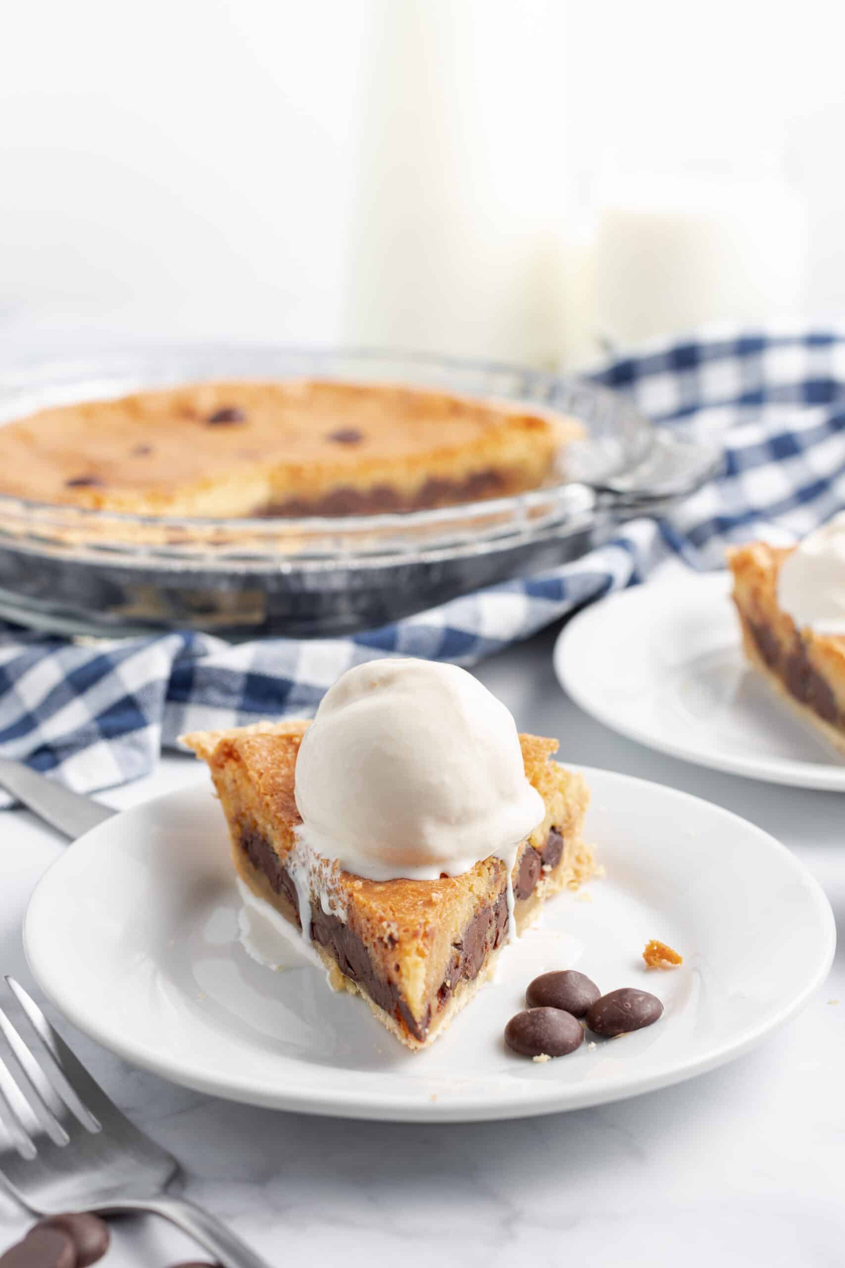 Slice of chocolate chip cookie pie on a white plate with a scoop of vanilla ice cream.