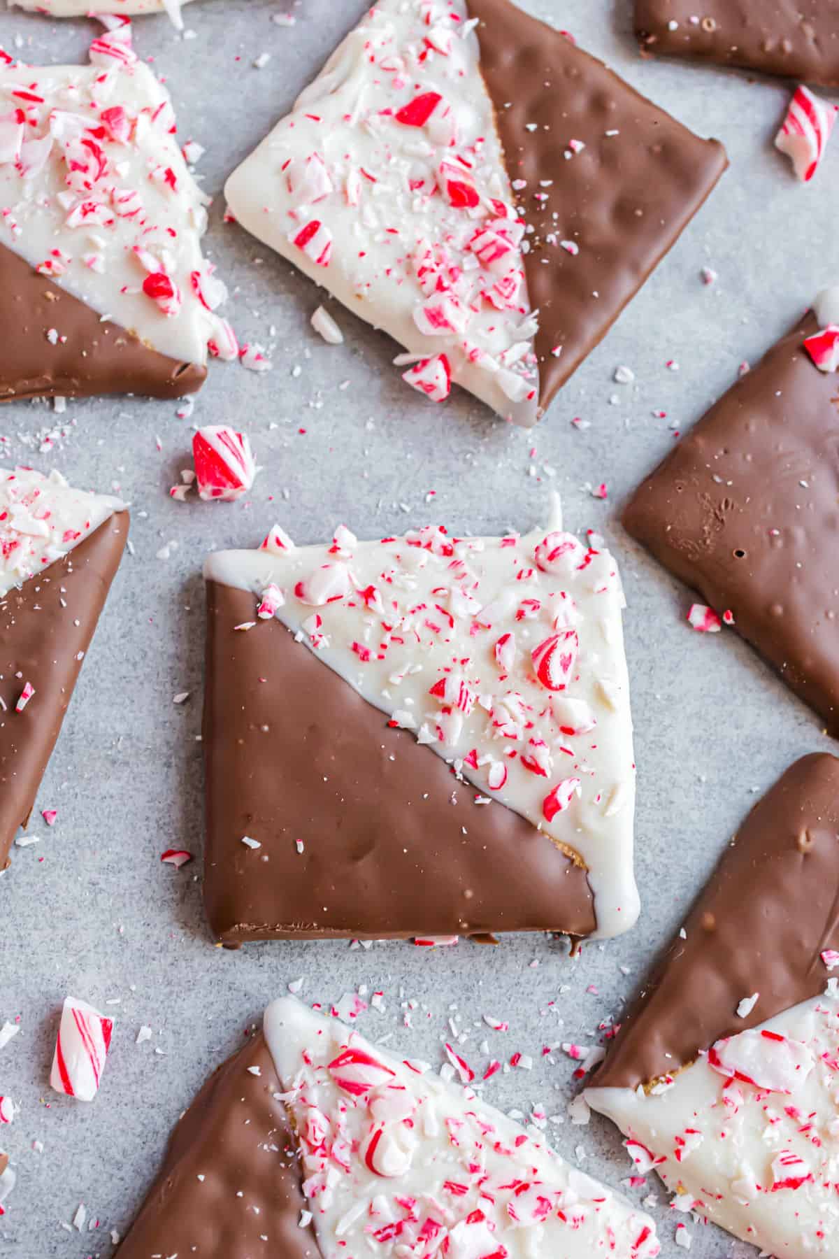 Milk chocolate and white chocolate dipped grahams with peppermint on parchment paper.