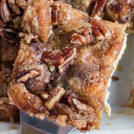 Eggnog french toast slice with pecans lifted out of pan.