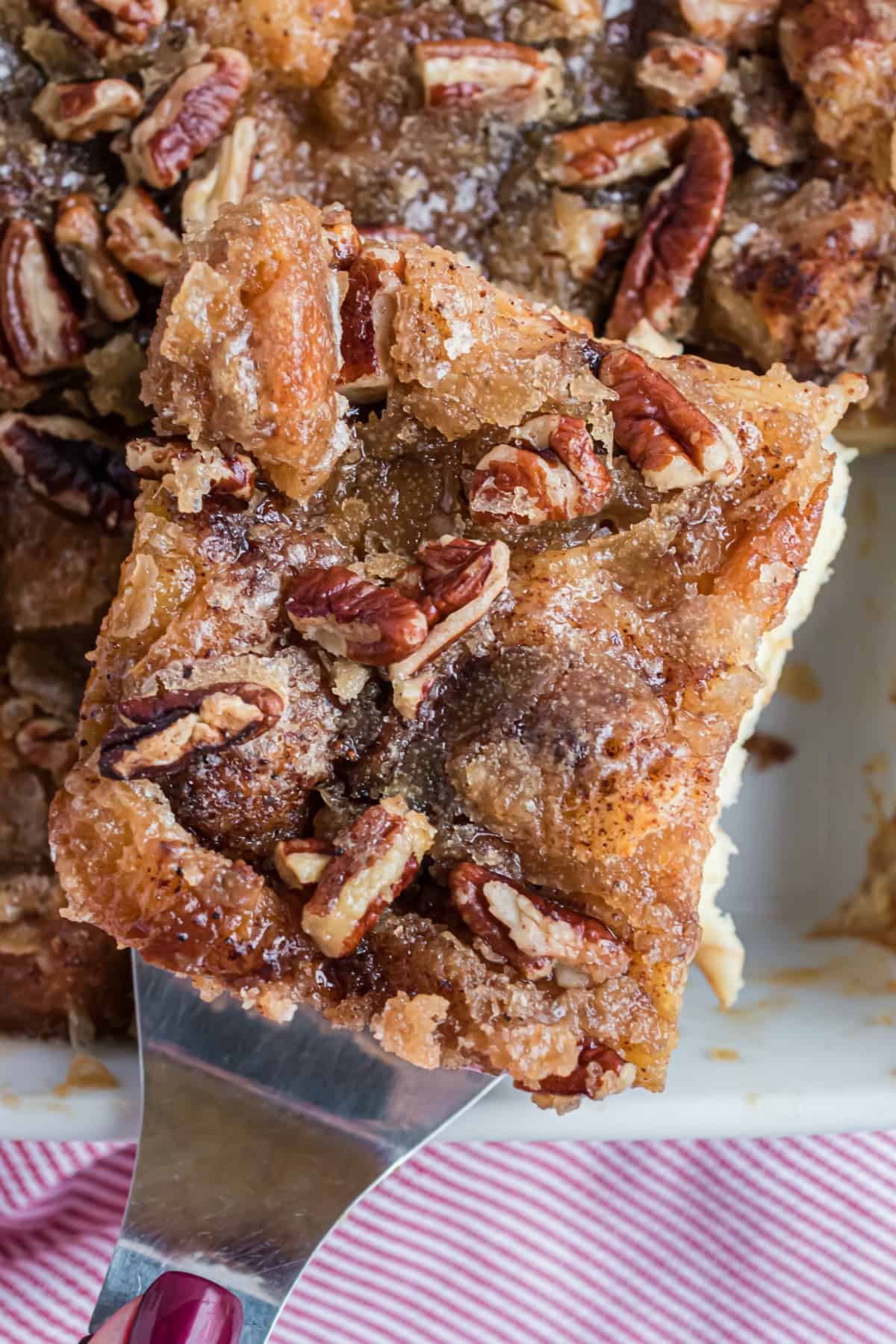 Eggnog french toast slice with pecans lifted out of pan.