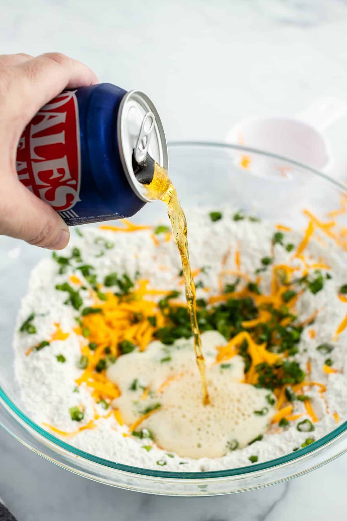 A can of beer being poured into a bowl of ingredients to make beer bread.