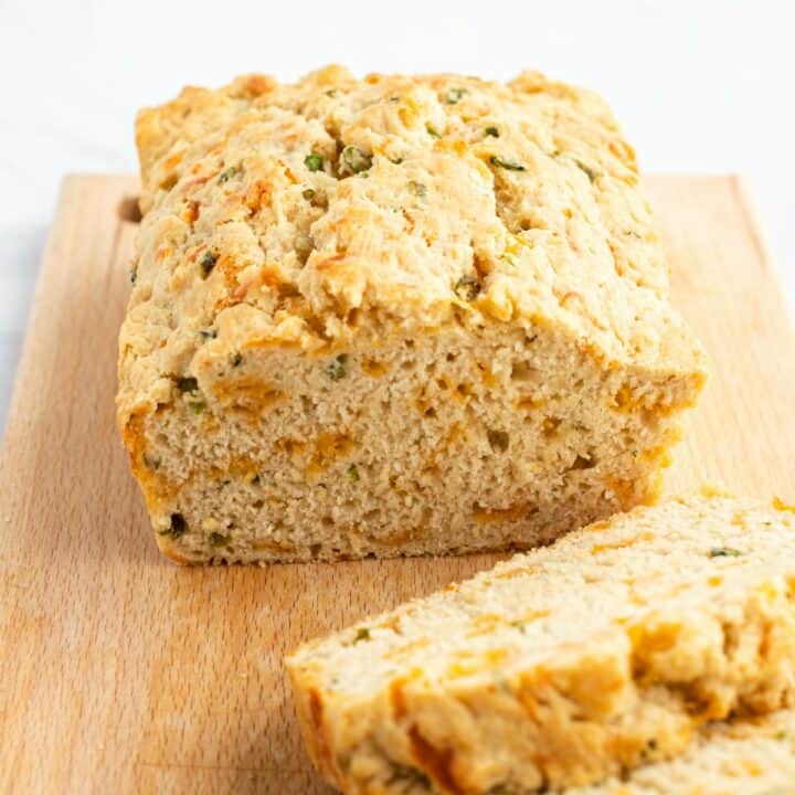 Beer bread with cheese and green onions on a wooden cutting board with several slices cut.