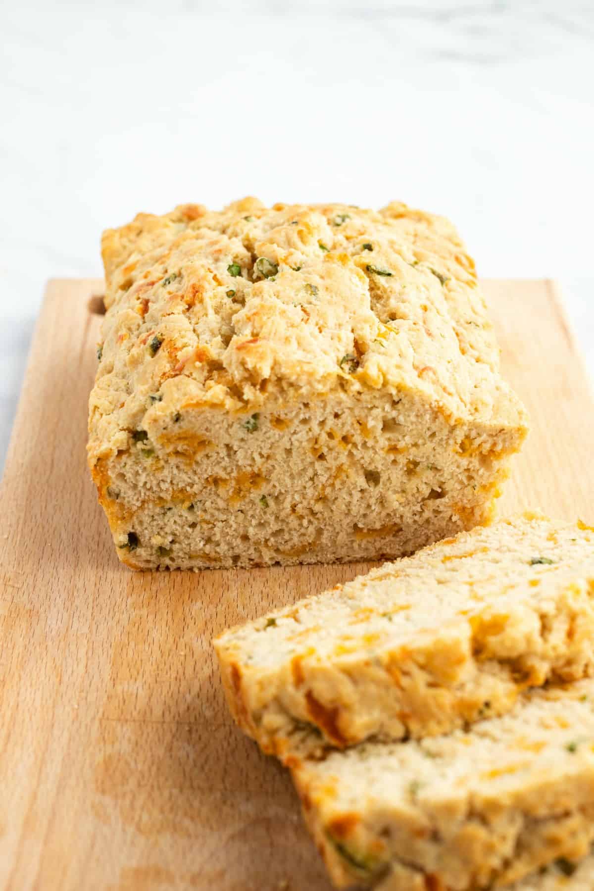 Beer bread with cheese and green onions on a wooden cutting board with several slices cut.