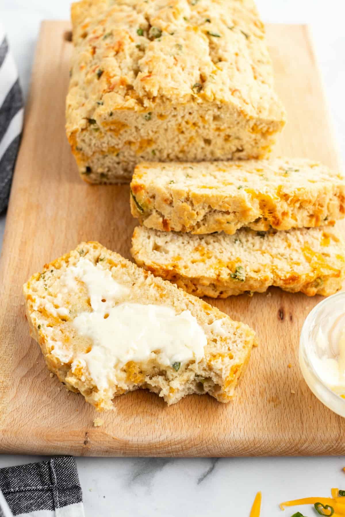 Sliced beer bread on a wooden cutting board slathered in butter.