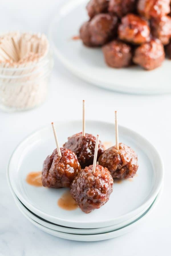 These Cocktail Meatballs (or Grape Jelly Meatballs) are exactly what your party needs, and they're super easy to make! Homemade Meatballs with an easy, two ingredient sauce. White plate with cocktail meatballs and toothpicks.
