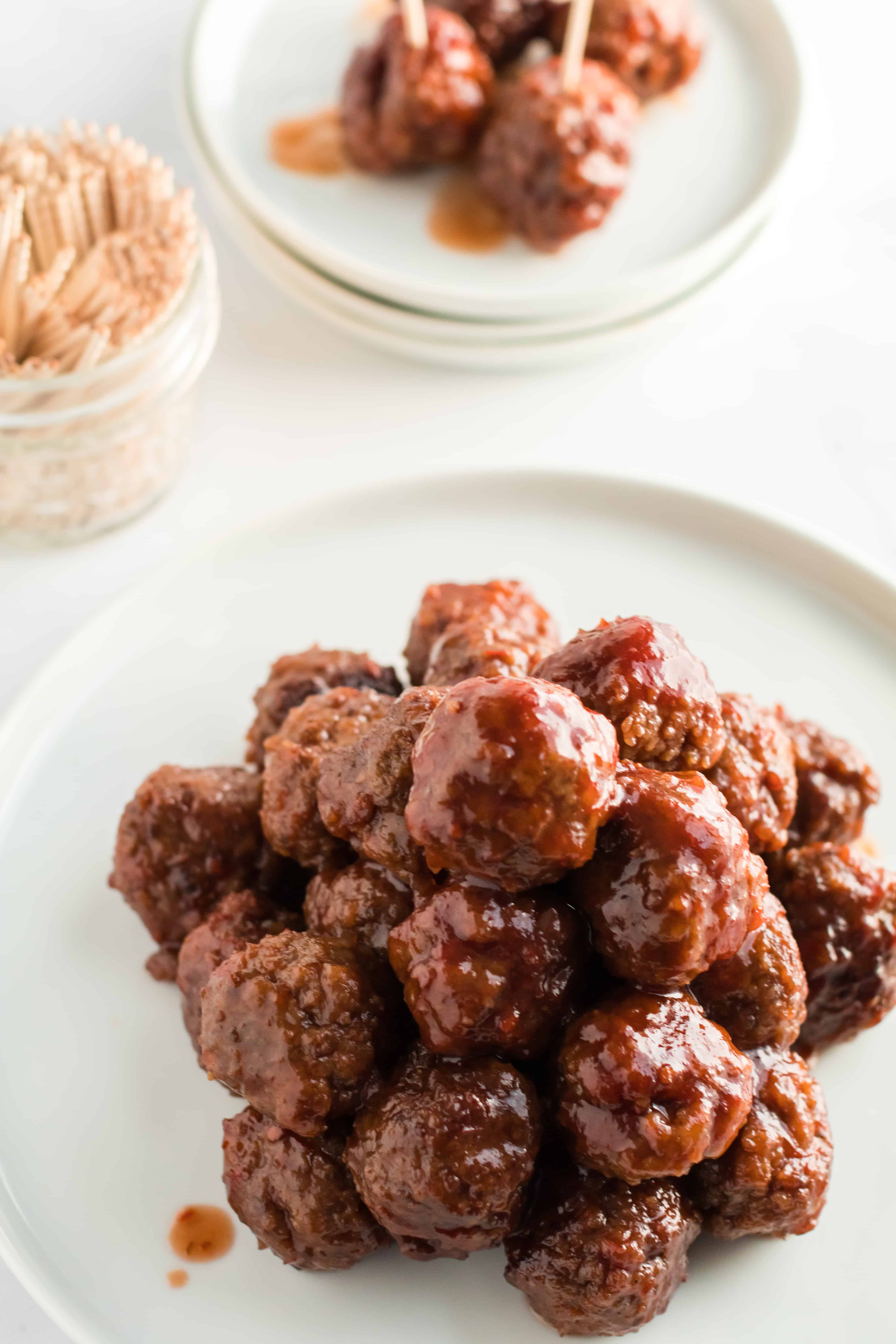 Meatballs on a white plate, stacked up with a jar of toothpicks in background.