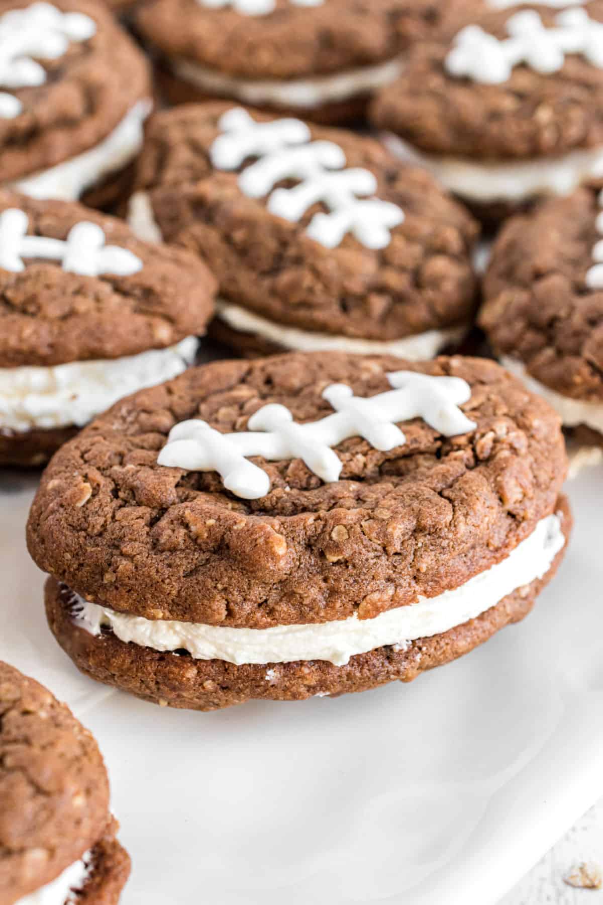 Football shaped oatmeal cream pies on white cake platter.