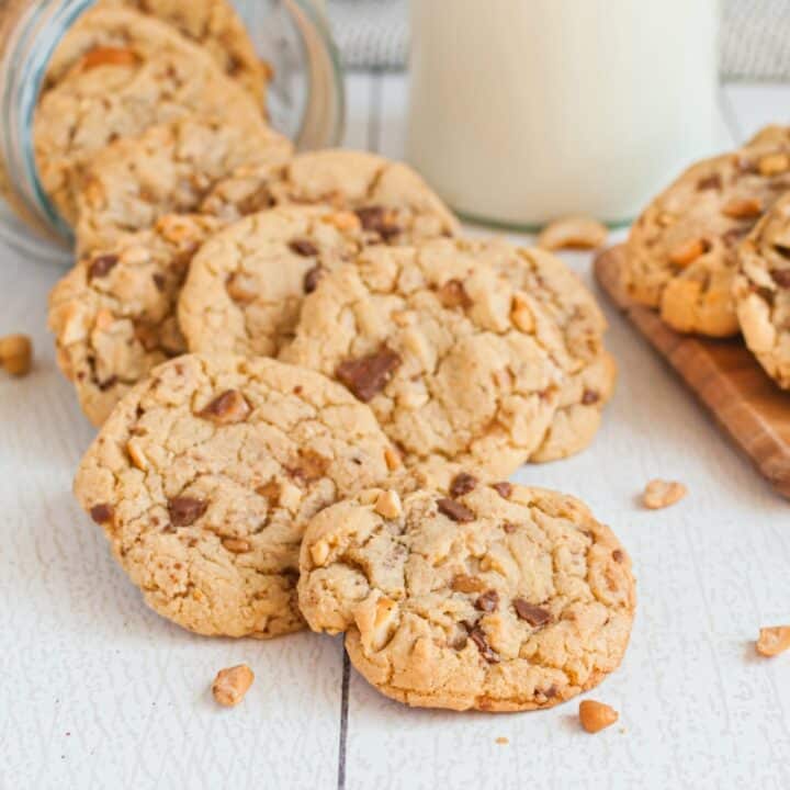 White wooden surface with toffee cashew cookies and jugs of milk.