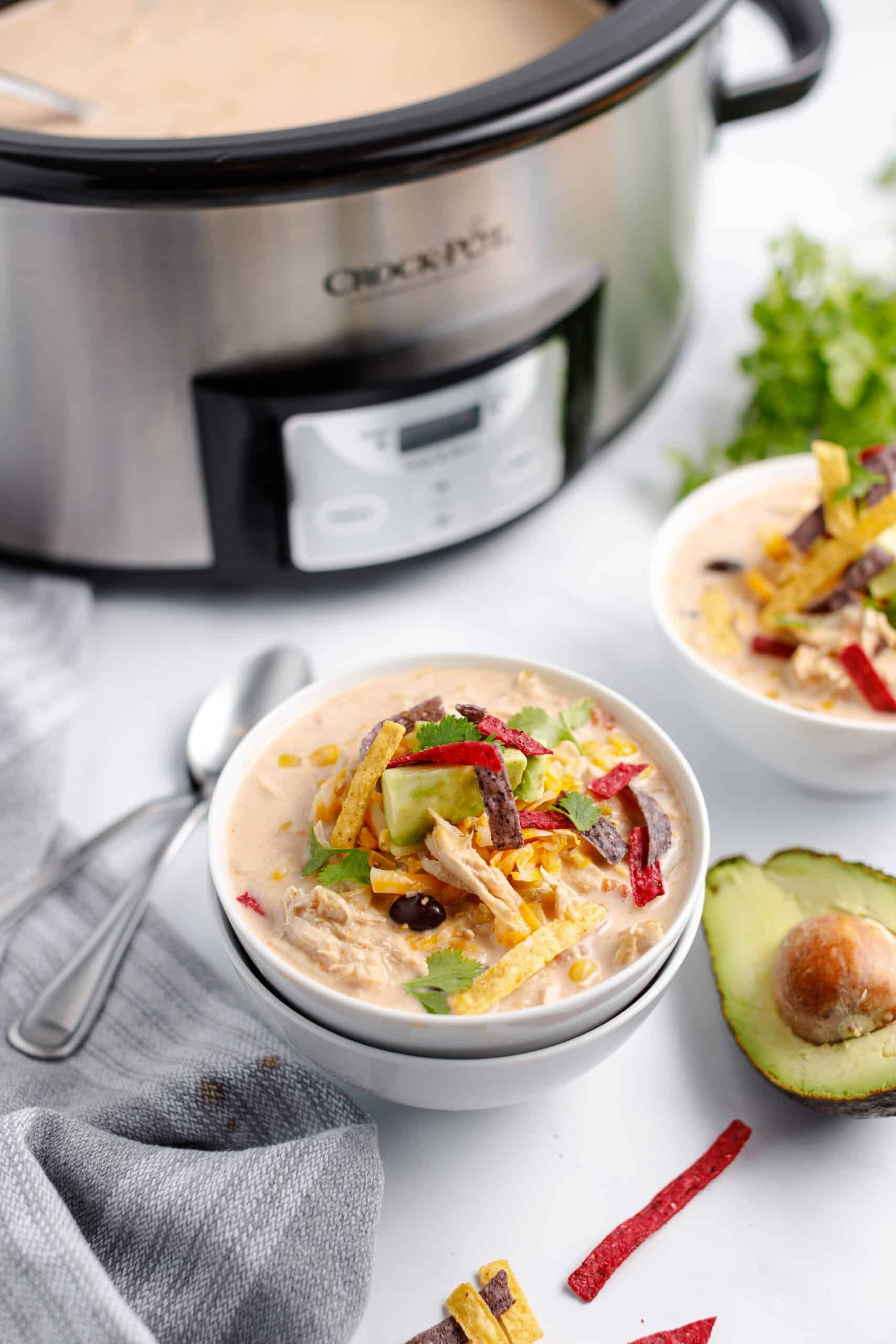 Turkey taco soup made in the crockpot. Two bowls stacked and topped with avocado, cheese, and tortilla strips.