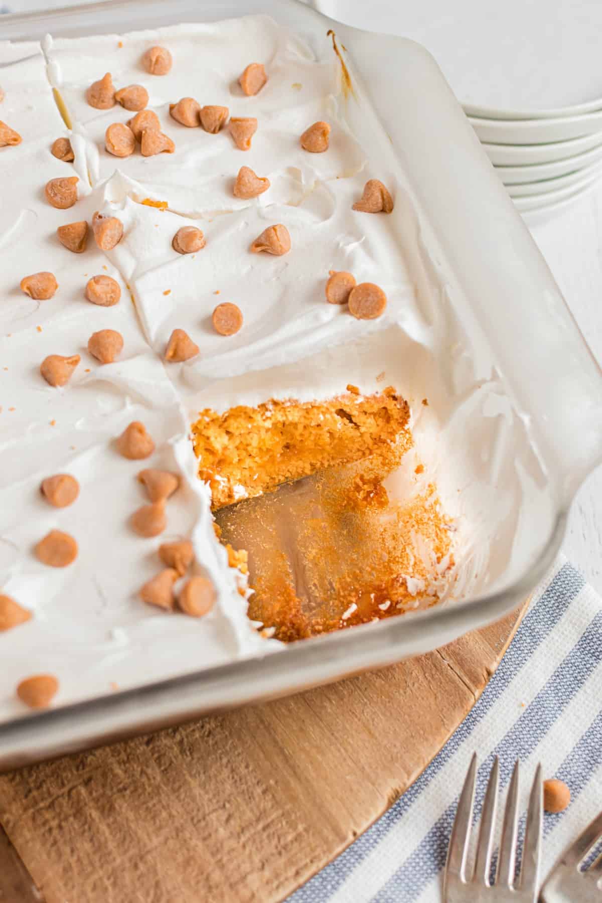 Glass 13x9 baking dish with a butterscotch pudding cake topped with cool whip, and one slice removed from the pan.