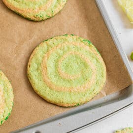 Lime swirled icebox cookies with green sprinkles on a parchment paper lined cookie sheet.