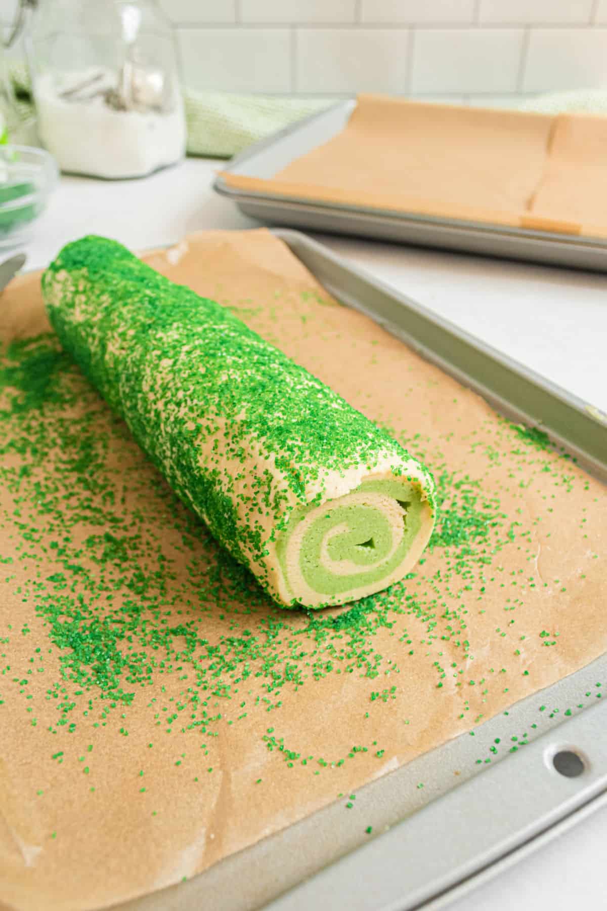 Lime swirled icebox cookies on parchment paper being rolled in sprinkles.