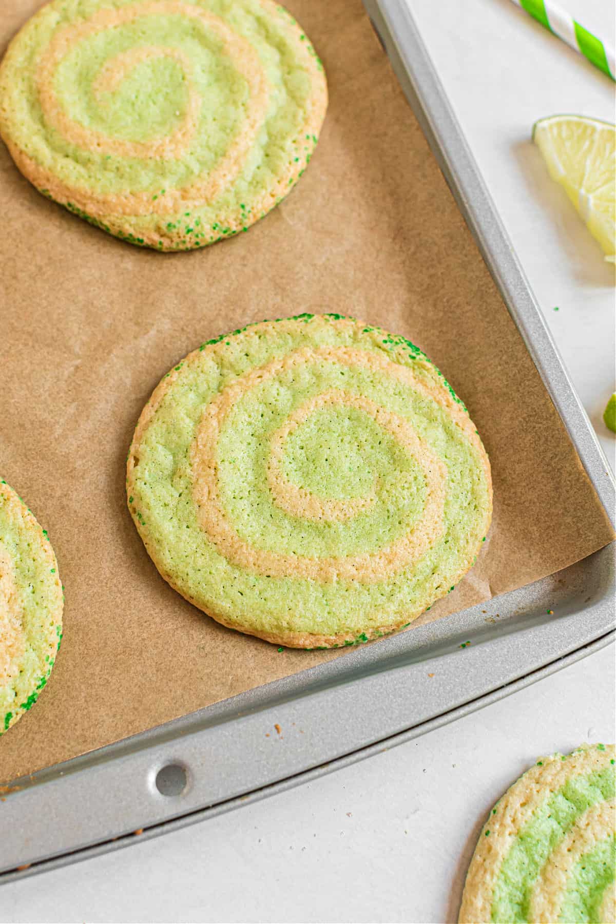 Lime swirled icebox cookies with green sprinkles on a parchment paper lined cookie sheet.