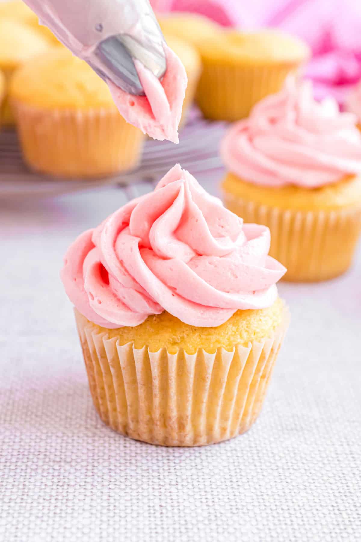 Cherry buttercream being piped onto an almond cupcake.