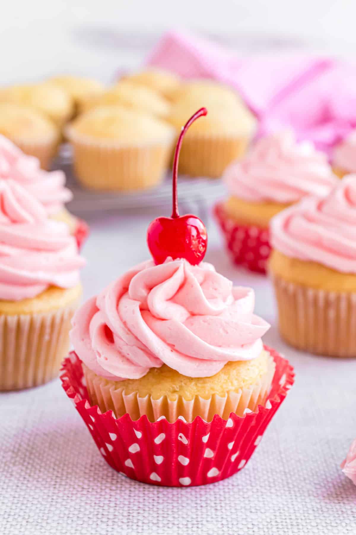 Almond cupcakes topped with cherry frosting and maraschino cherries.