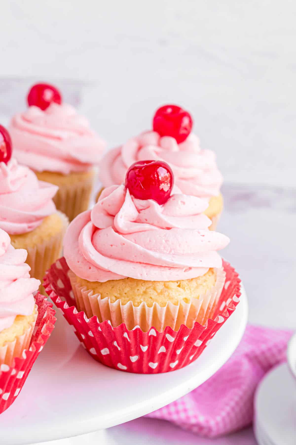 Cherry almond cupcakes on a white cake plate.