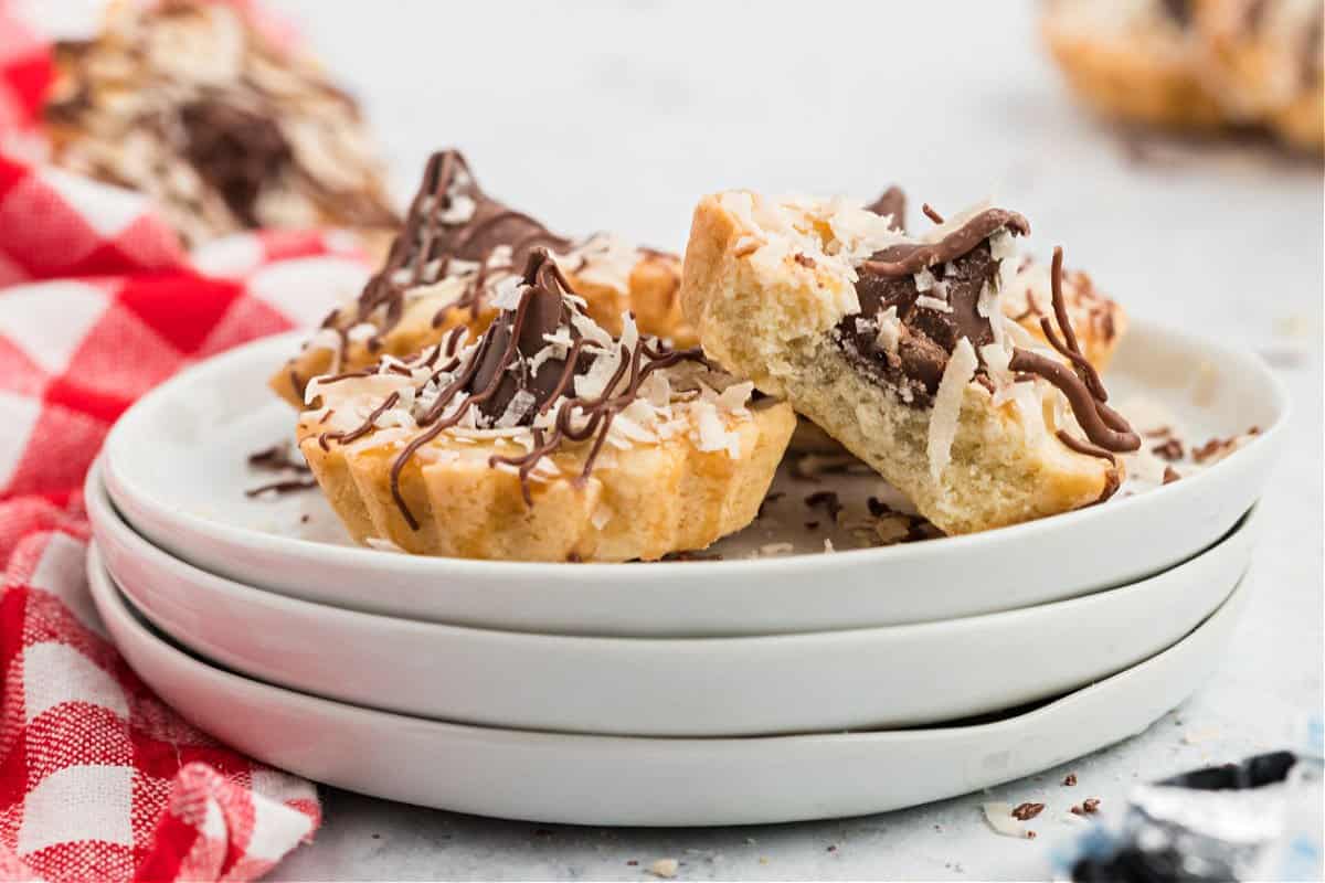 Two coconut kiss cookies on a stack of white plates.