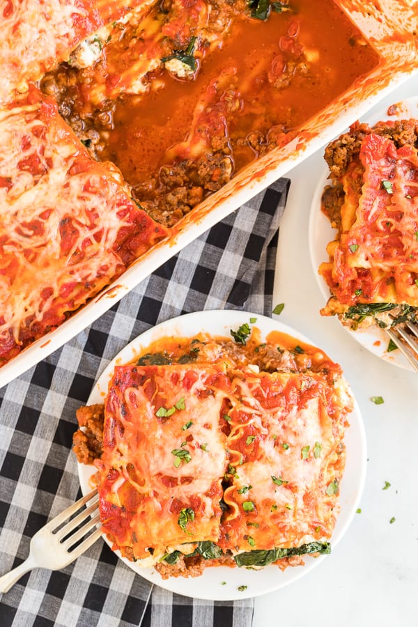 Overhead view of spinach and meat lasagna being served on two white dinner plates.