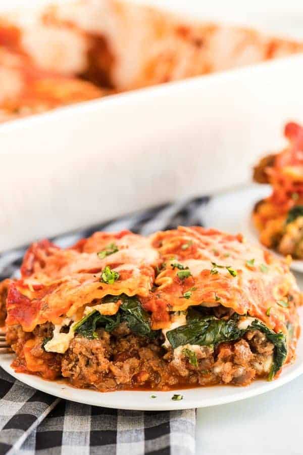 Big slice of Spinach and Meat lasagna on white plate with black and white checkered napkin.