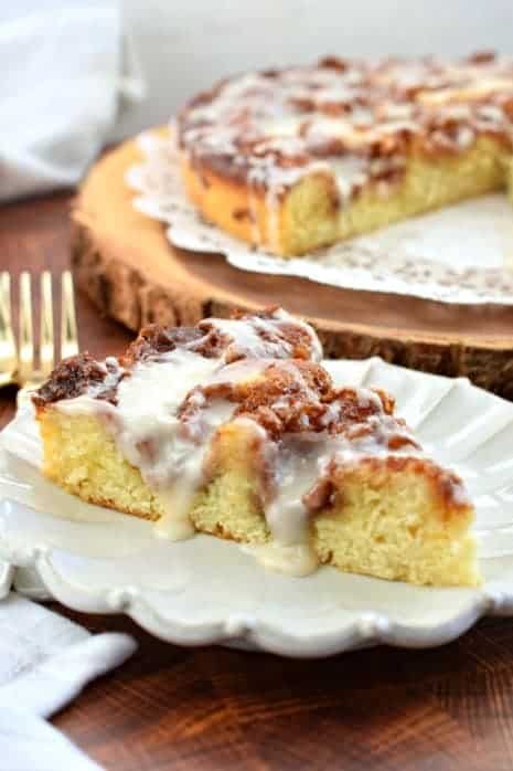 Slice of Cinnabon Cinnamon Roll cake with dripping vanilla glaze on white scalloped plate.