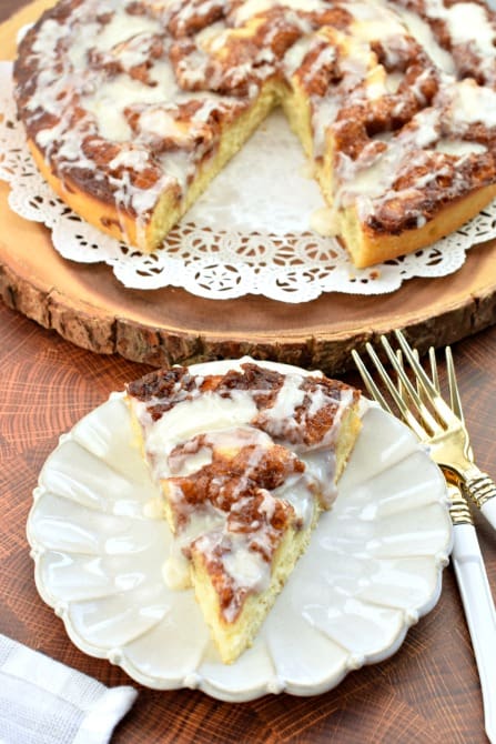 Pie shaped slice of cinnamon roll cake on a white plate.