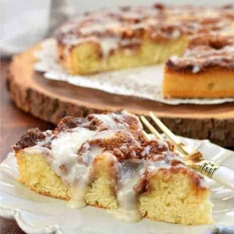 Slice of cinnamon roll cake on a white plate with whole cake in background.