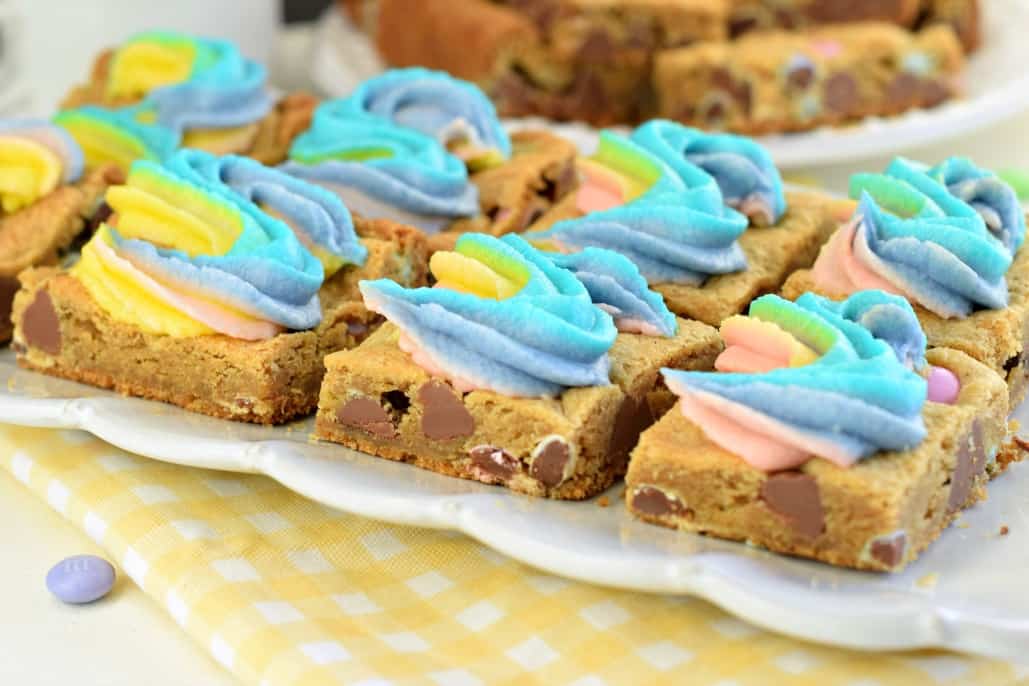 White scalloped plate with squares of rainbow frosted cookie bars.