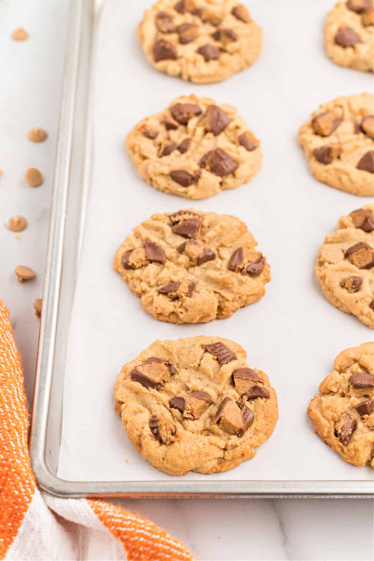 Peanut butter cookies with reese's peanut butter cups on a parchment paper lined cookie sheet.