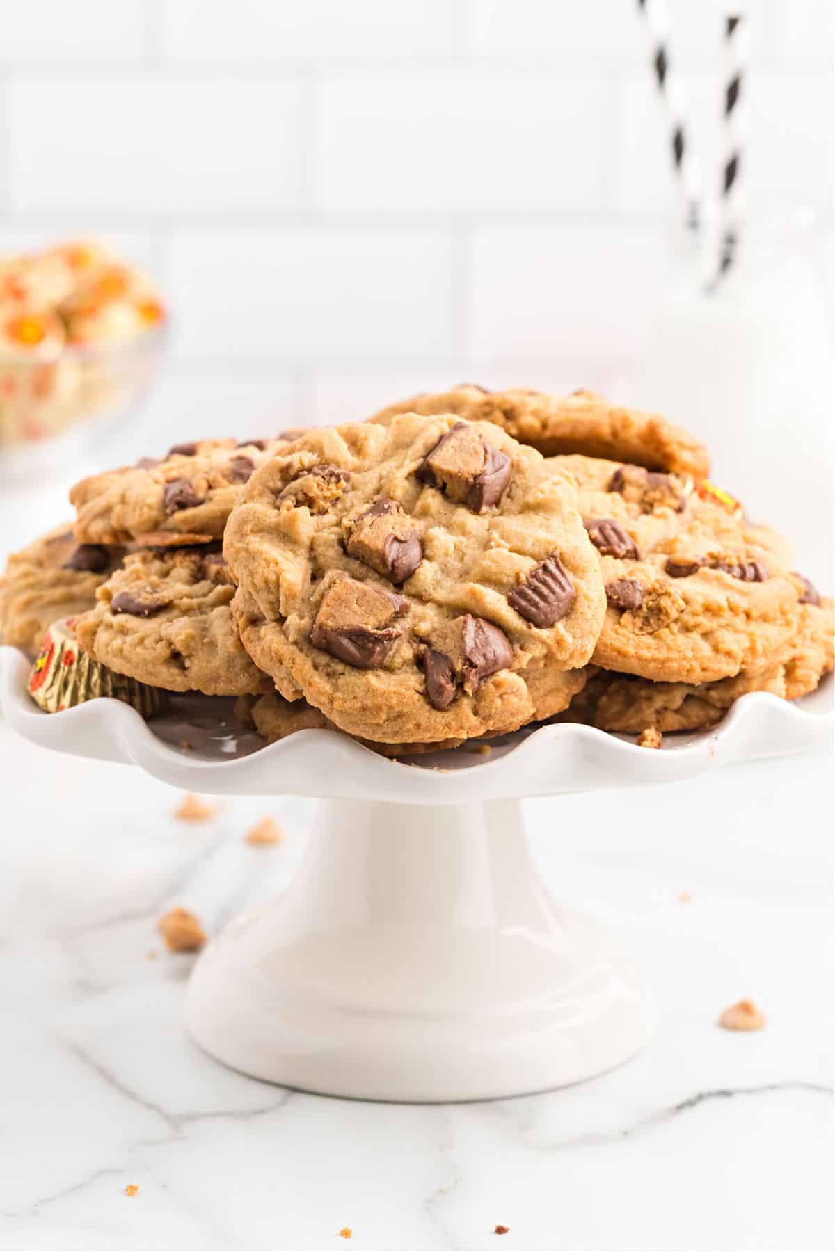 White cake plate with peanut butter cup cookies stacked on top.