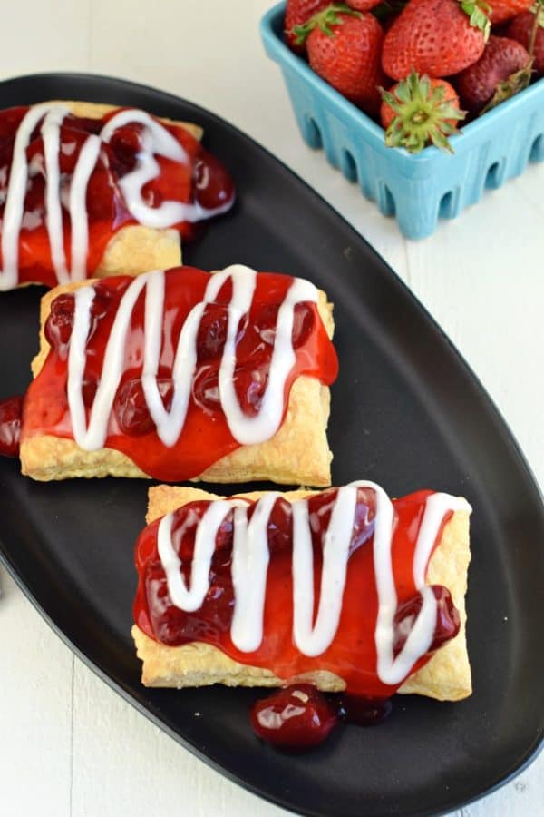 Strawberry topped toaster strudels on a black oval platter.
