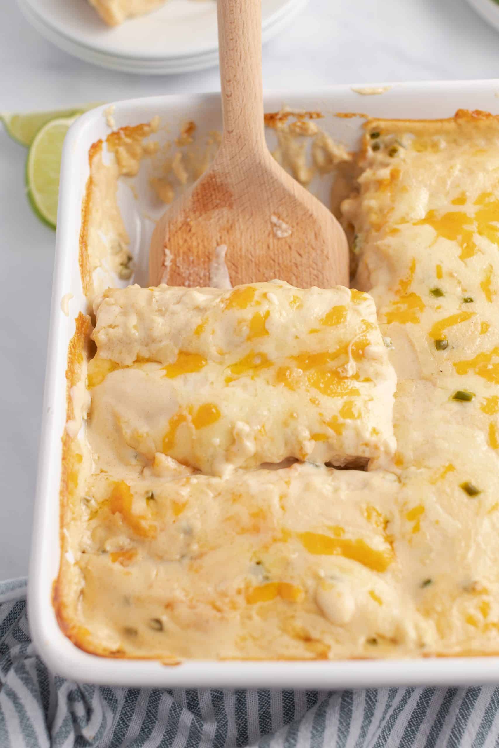 Pan of cream chicken enchiladas with wood spatula