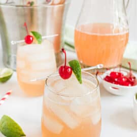 Cherry margaritas in a glass garnished with lime and maraschino cherries.