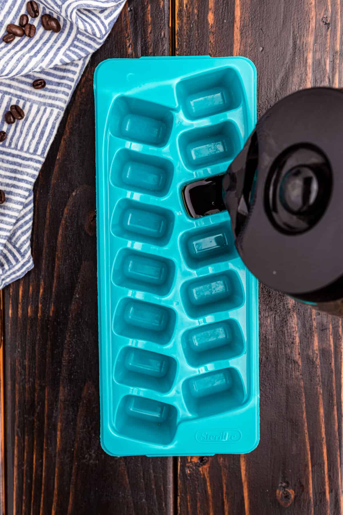 Brewed coffee being poured into a blue ice cube tray.