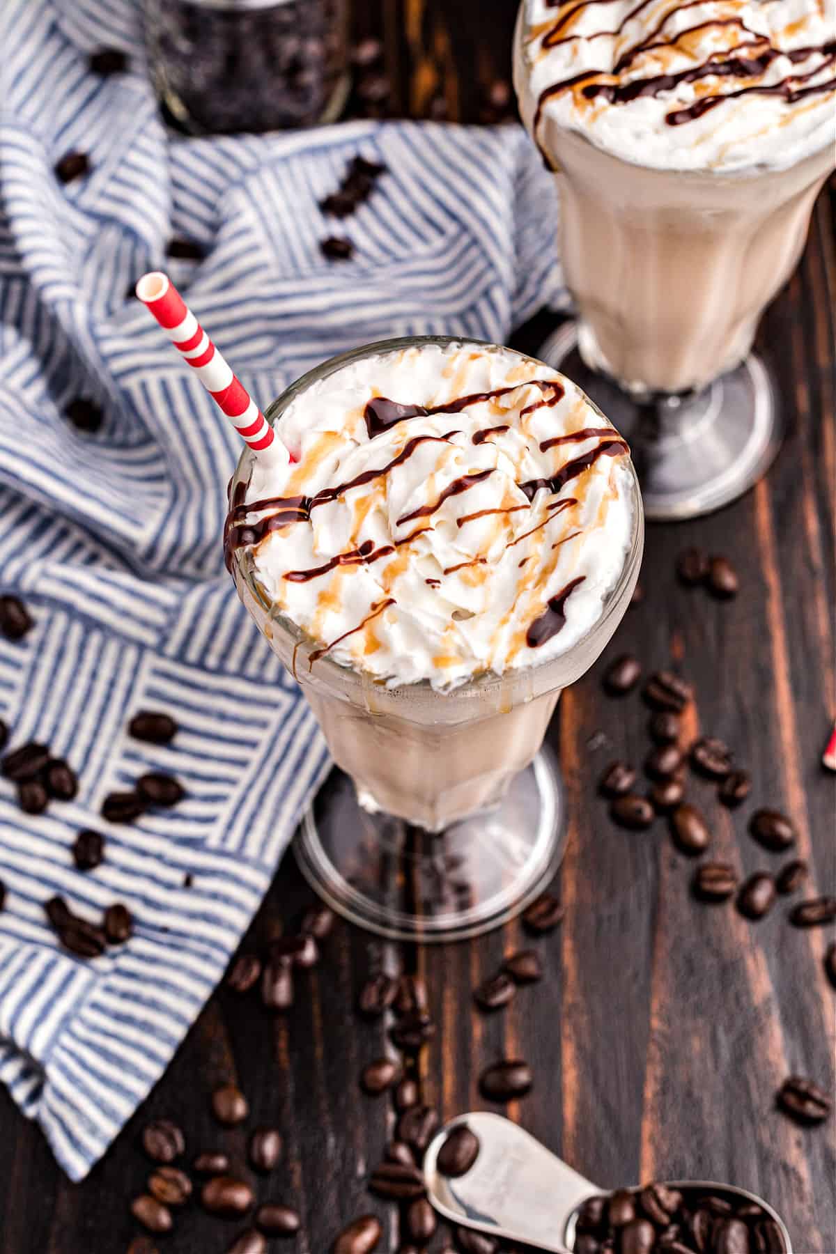 Two tall glasses of coffee milkshakes topped with drizzles of caramel and chocolate sauce.