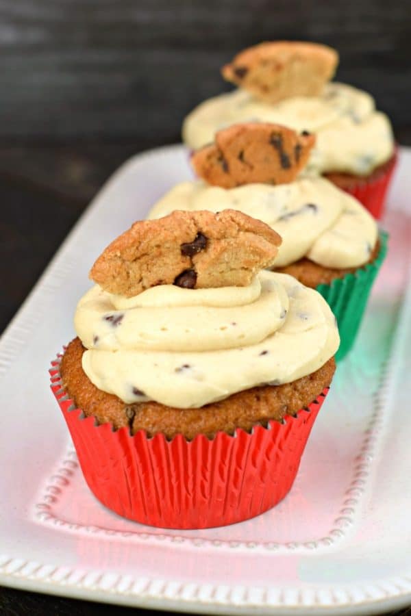 Three Chocolate chip cupcakes with cookie dough frosting on a rectangular plate, topped with a cookie