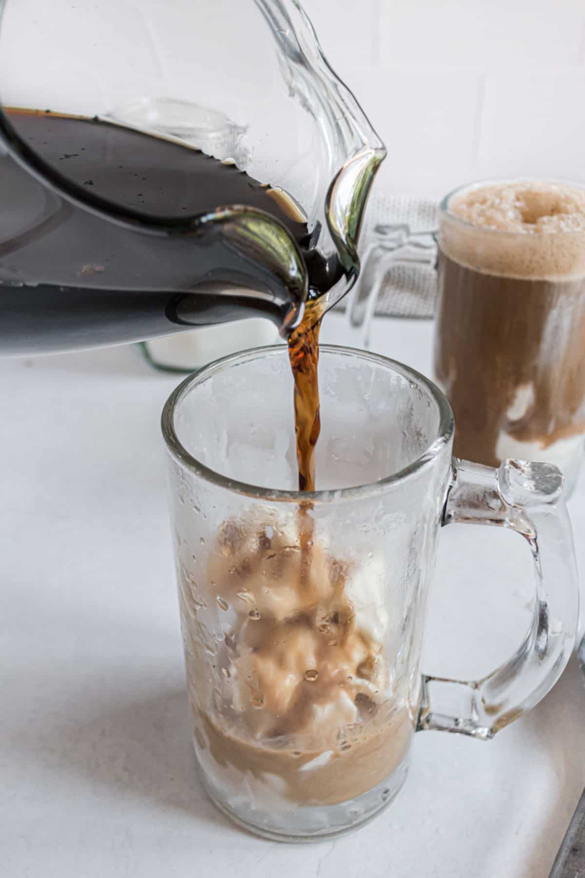 Homemade root beer being poured into a tall glass with vanilla ice cream.