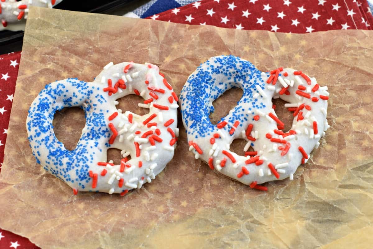 Two red white and blue white chocolate covered pretzels on a piece of parchment paper.