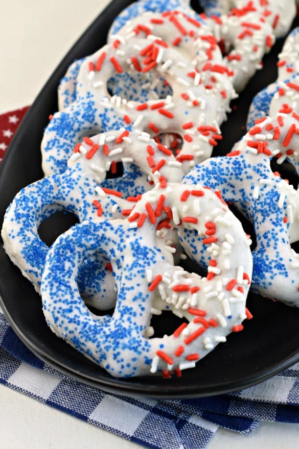 White chocolate covered pretzels with red white and blue sprinkles on a black serving plate.