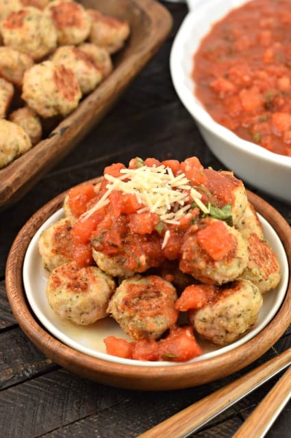 Turkey meatballs on a plate with bruschetta sauce. Bowl of meatballs and bowl of sauce in background.