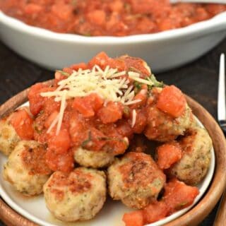 Pile of turkey meatballs on a white plate topped with bruschetta sauce and parmesan cheese.