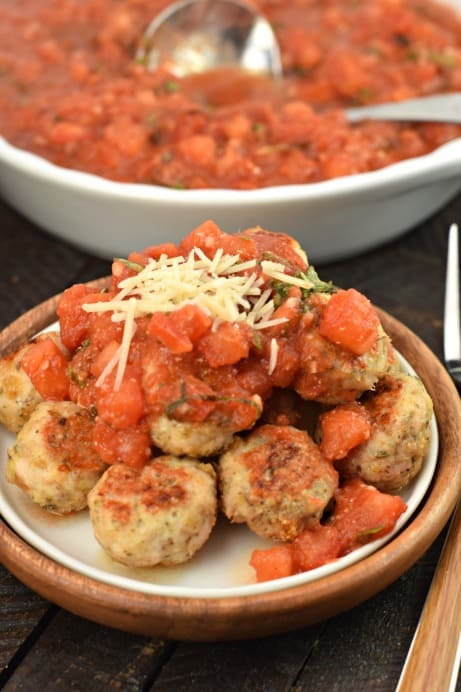 Pile of turkey meatballs on a white plate topped with bruschetta sauce and parmesan cheese.