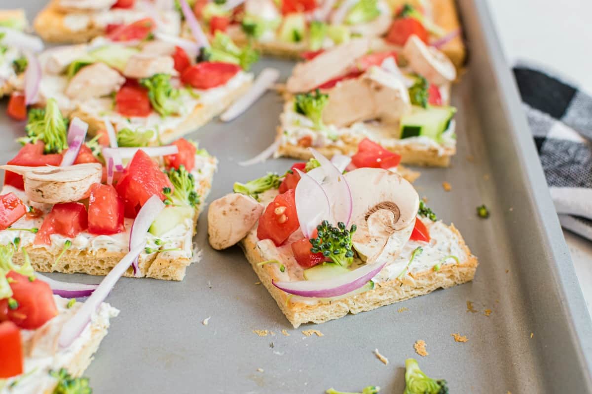 Veggie pizza cut into squares on a metal baking sheet.